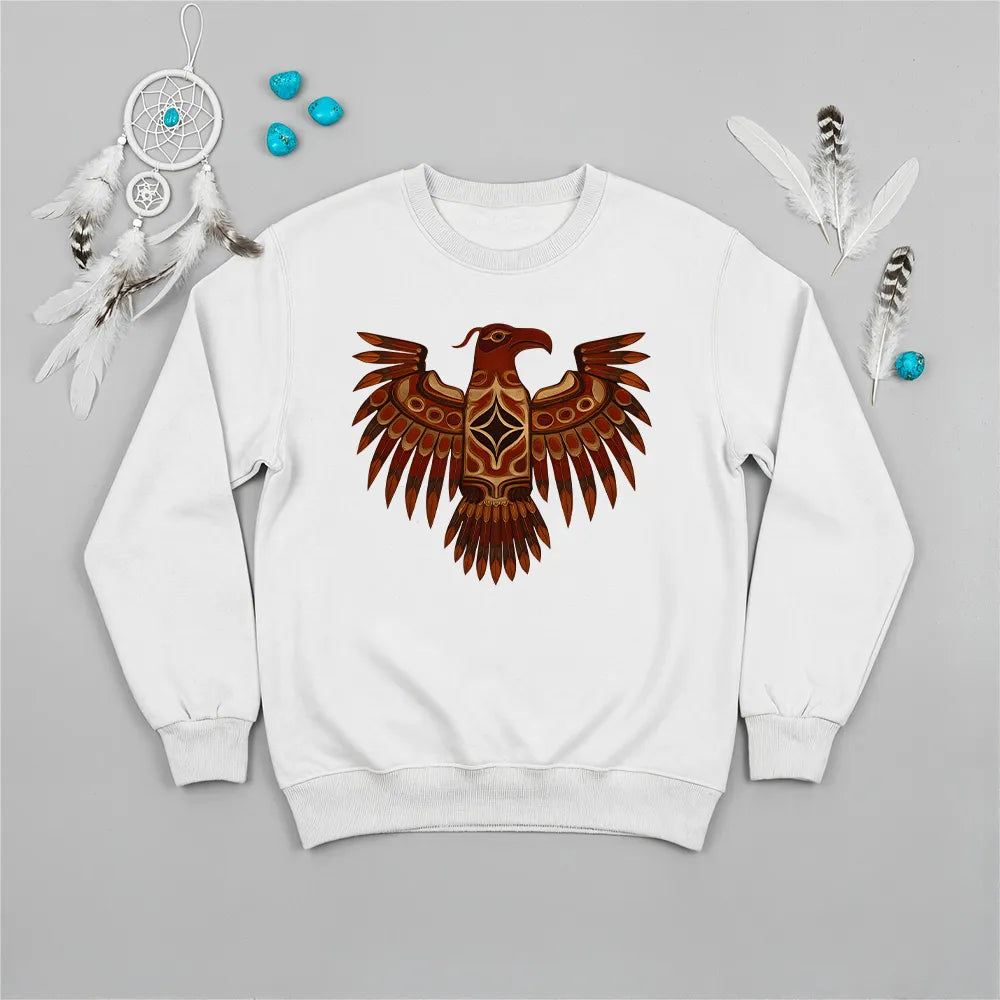 A red crewneck sweatshirt featuring a traditional Native American Thunderbird design, laid flat with a dreamcatcher and feathers.