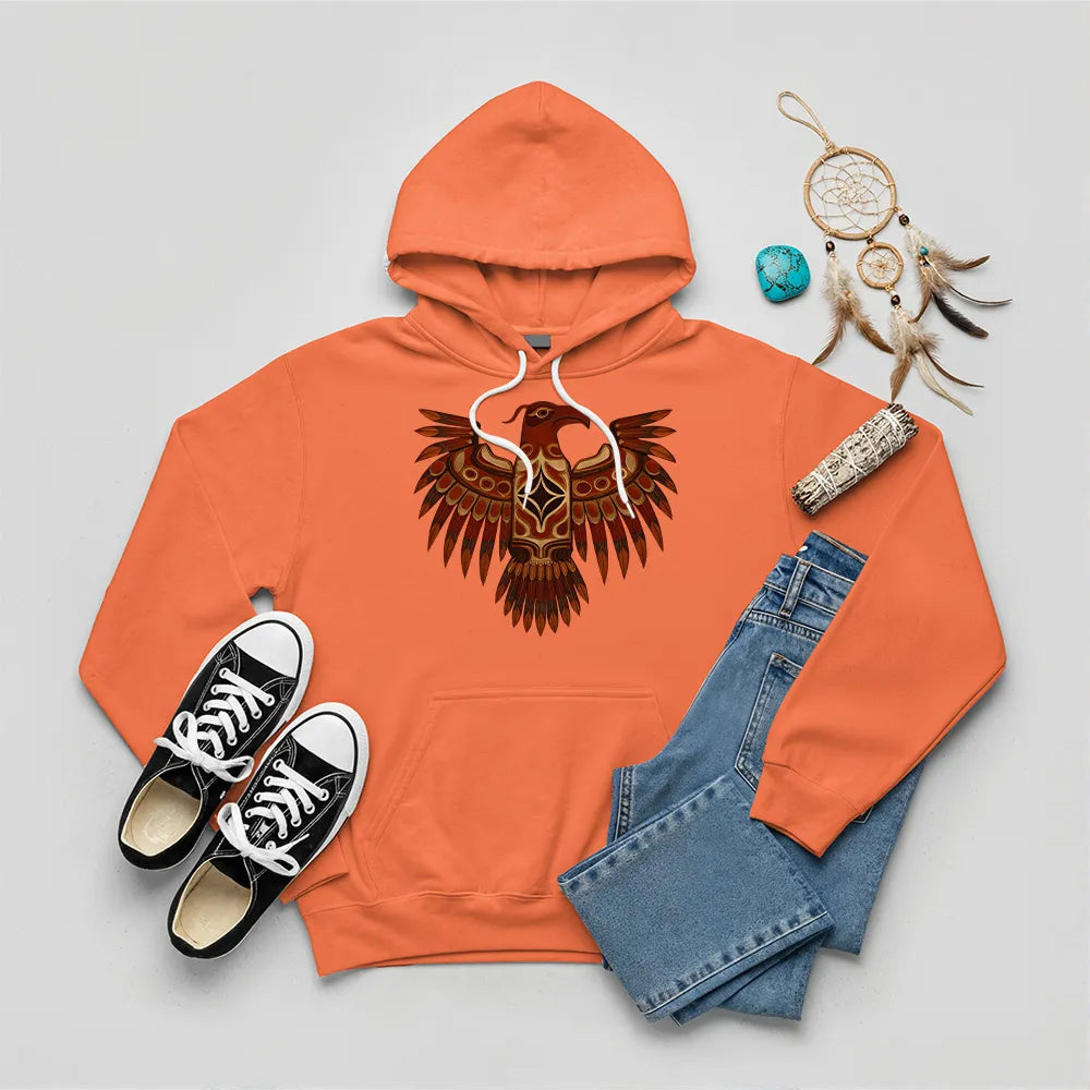 An orange hoodie featuring a striking indigenous Thunderbird pattern, arranged with denim pants and sneakers.