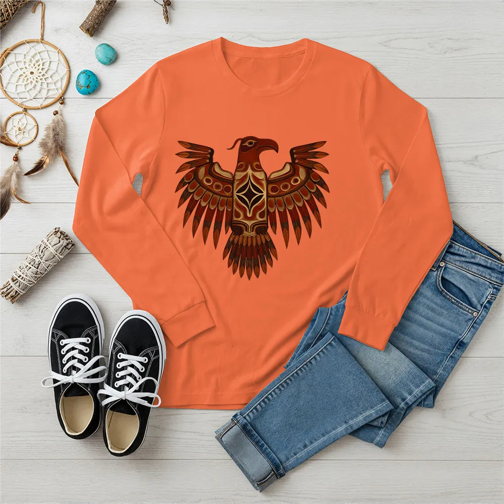 An orange long-sleeve t-shirt featuring a striking indigenous Thunderbird pattern, arranged with denim pants and sneakers.