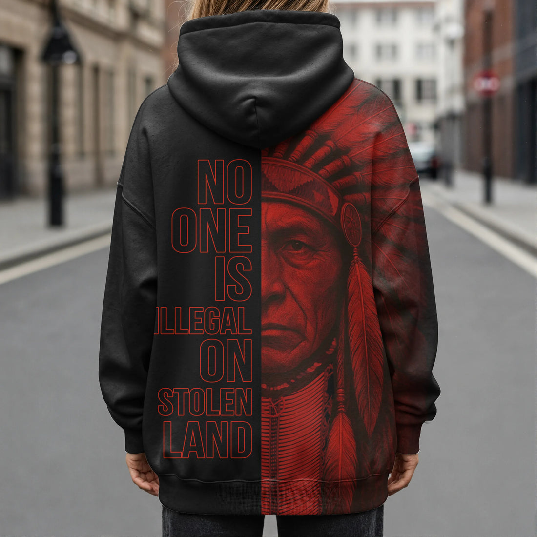 Model photographed from the back wearing a black and deep-red fleece hoodie with the bold slogan “NO ONE IS ILLEGAL ON STOLEN LAND” printed down the center