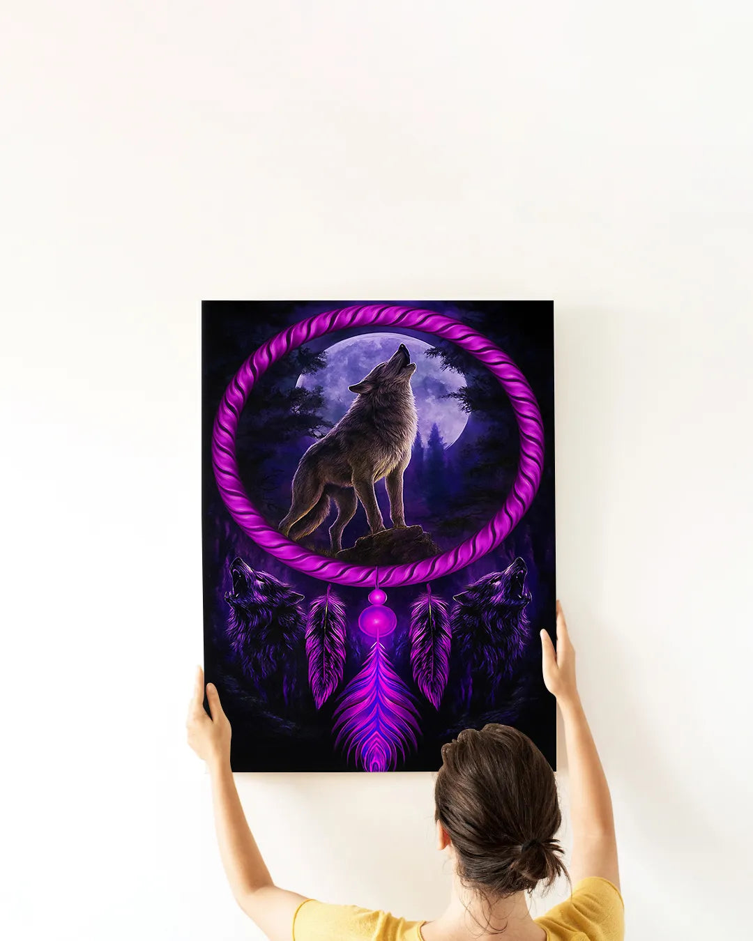 A woman’s hands hanging a framed canvas print featuring a purple wolf howling inside a dreamcatcher ring against a moonlit forest backdrop.