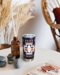 20 oz insulated stainless steel tumbler with navy Aztec cross pattern sitting on a white tabletop next to decorative stones and a reed diffuser.