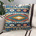 Square teal, rust and gold Aztec pattern throw pillow resting on a cream sofa next to a large leafy plant.