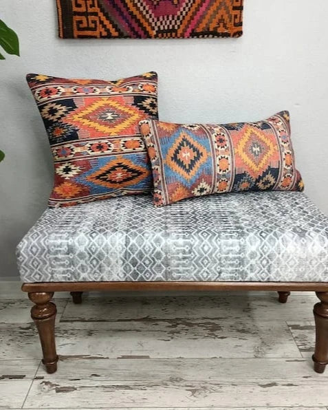 Square and lumbar Southwestern Aztec pattern throw pillows in rust and navy resting on a patterned bench with a leafy plant in the background.