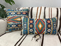 Square and matching lumbar teal, rust and gold Aztec pillows arranged together on a striped woven couch.