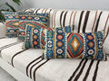 Southwestern Aztec pattern pillows—two square and one lumbar—in teal, rust and gold hues displayed on a cozy sofa.