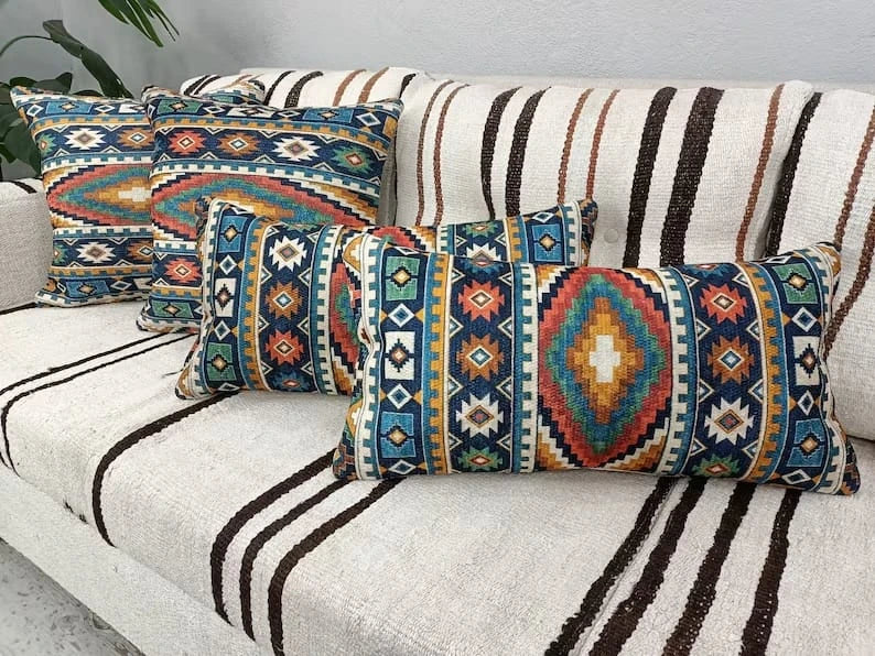 Southwestern Aztec pattern pillows—two square and one lumbar—in teal, rust and gold hues displayed on a cozy sofa.