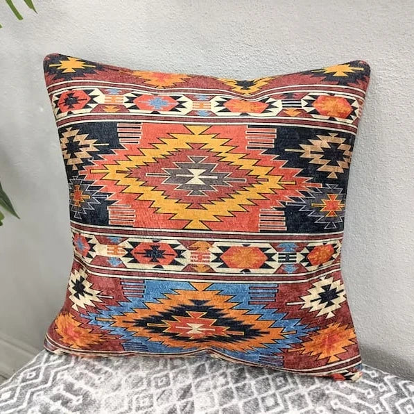Square and lumbar Southwestern Aztec pattern throw pillows in rust and navy resting on a patterned bench with a leafy plant in the background.