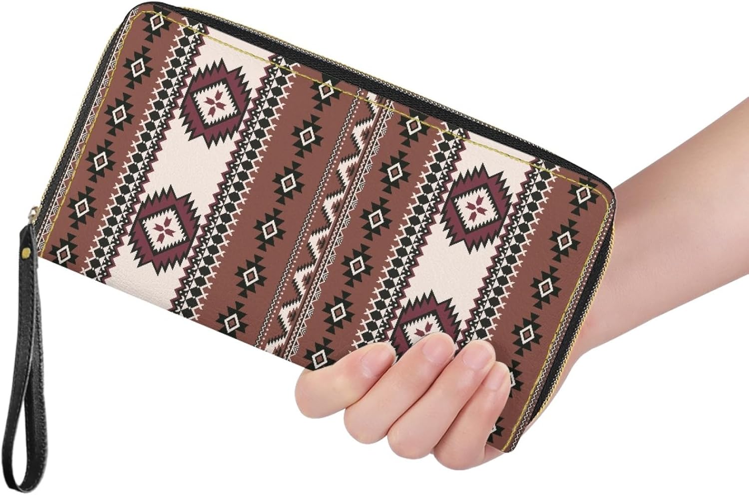 A hand holding the brown patterned wristlet wallet against a white background, showcasing its size and detailed tribal-inspired print.
