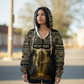 Front of a black zip-up hoodie with gold geometric tribal designs on the hood and shoulders, showing the same Native elder flute-player and buffalo skull artwork across the chest, a full-length zipper, and kangaroo pockets, embodying a vintage Indigenous pride aesthetic.